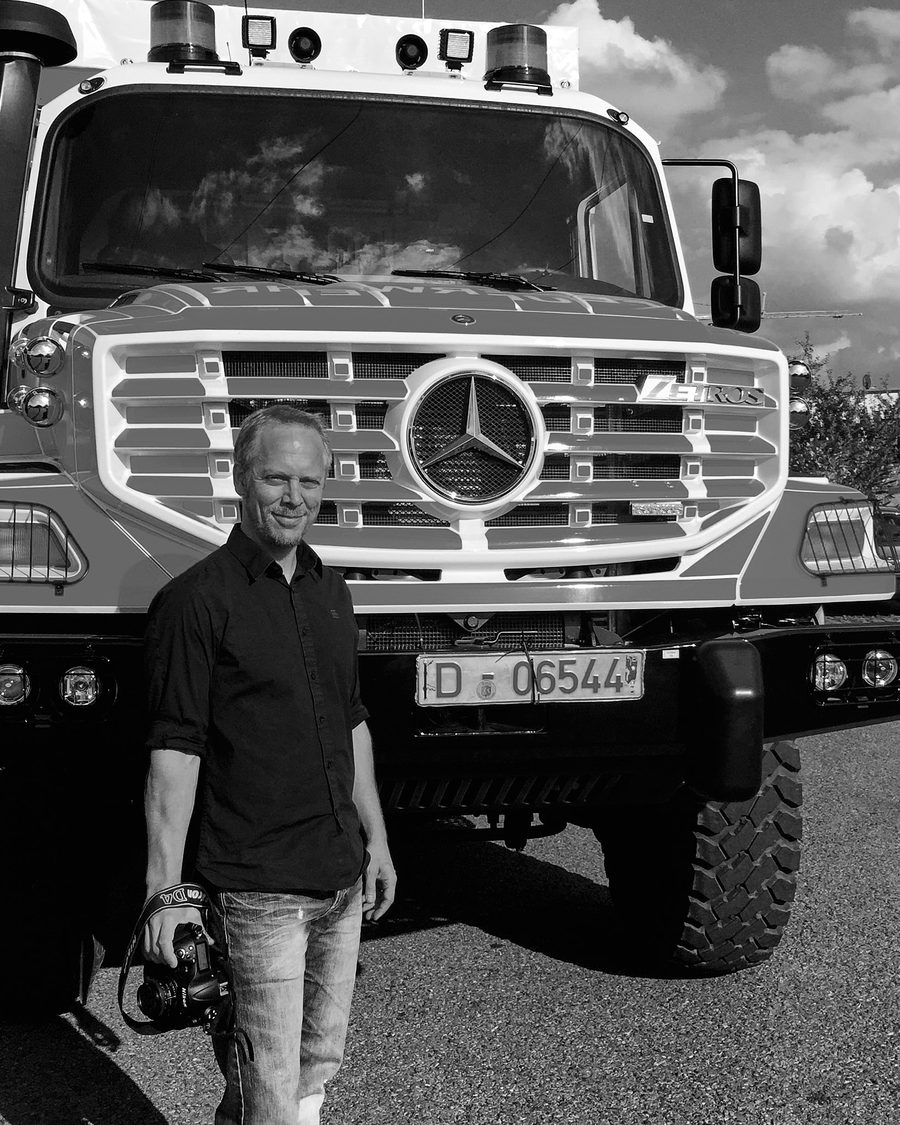Svartvitt porträtt av Jonas Eriksson, fotograf på siljanfoto, med kameran framför en lastbil.